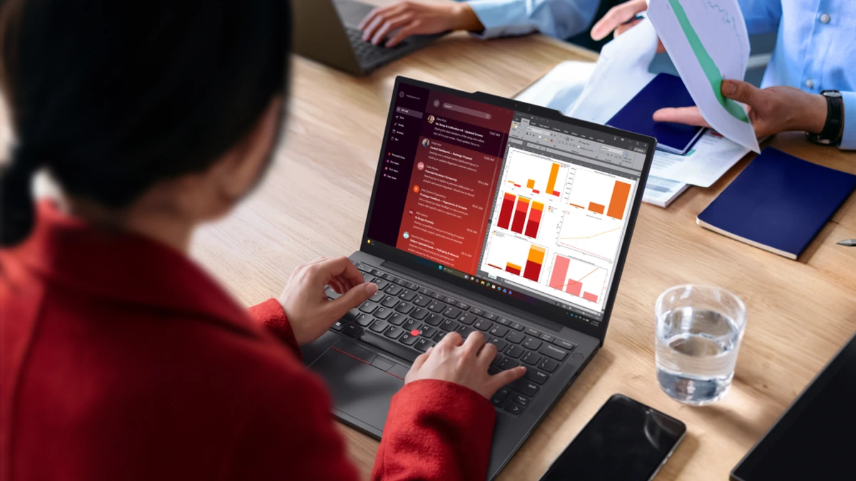 Woman in red working on a Lenovo ThinkPad laptop showing charts at a meeting table with colleagues