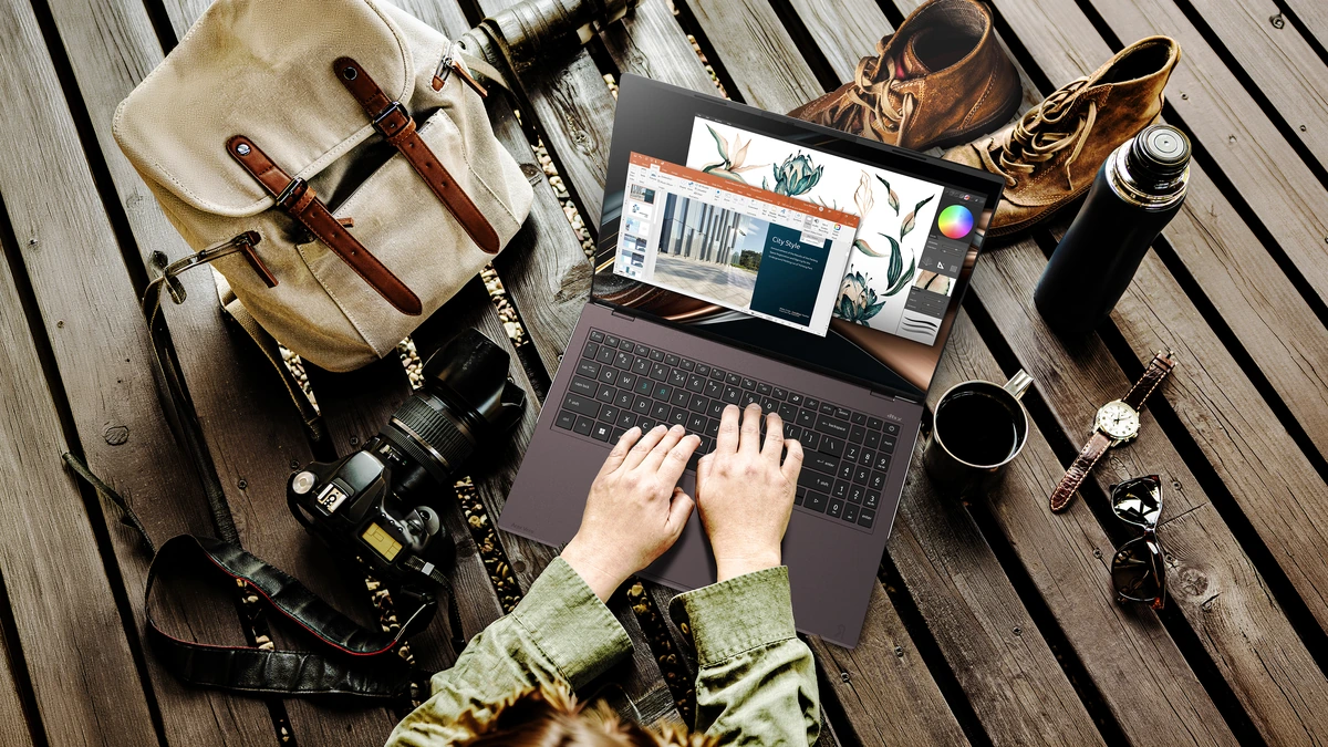 Overhead view of hands typing on the Acer Vero 16 laptop on wood decking, beside a backpack, camera and boots