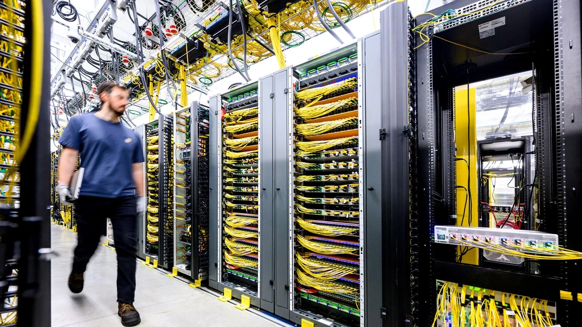 A technician walks past rows of server racks with yellow cabling in an Amazon data center
