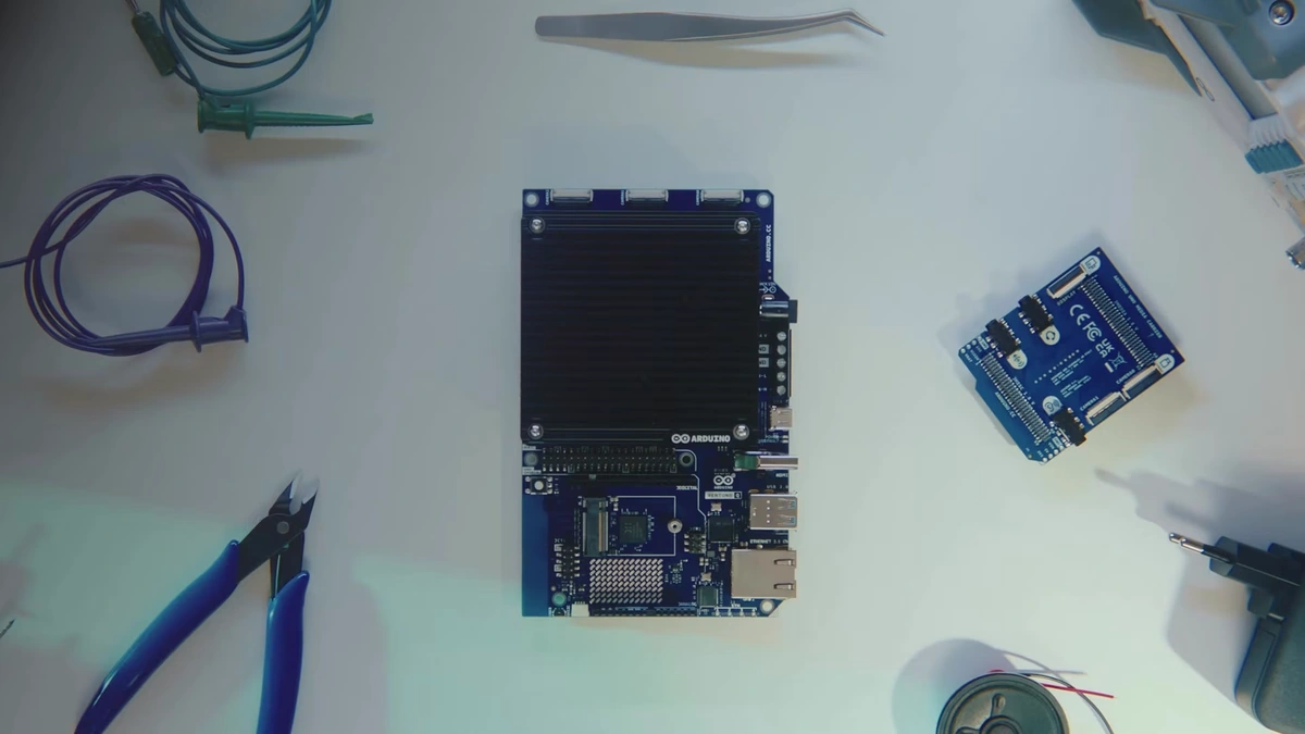 Arduino VENTUNO Q board with a black heatsink on a white workbench beside a carrier board, pliers and cables