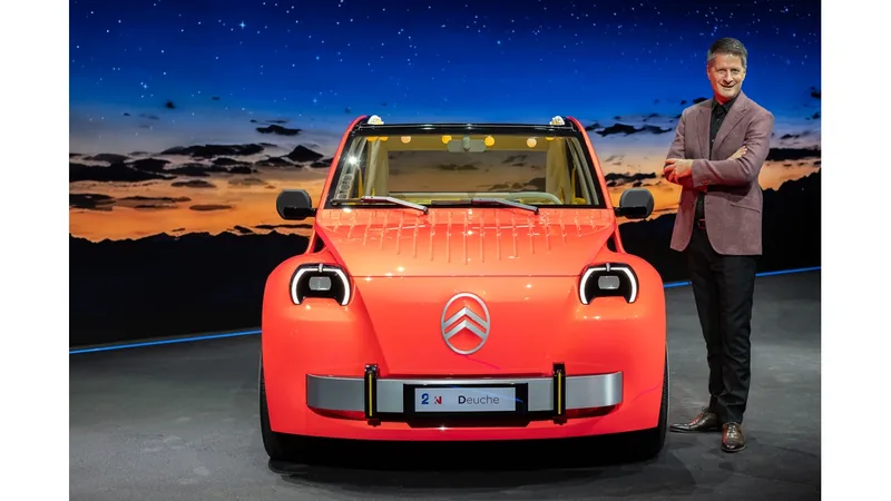 2 CV Concept electric car in bright orange on a show stage, with a man in a blazer standing beside it