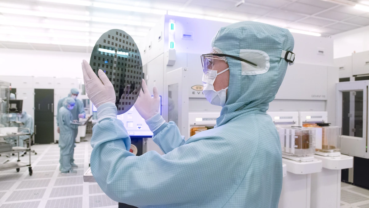 A cleanroom technician in a blue bunny suit inspects a patterned semiconductor wafer at an EV Group facility