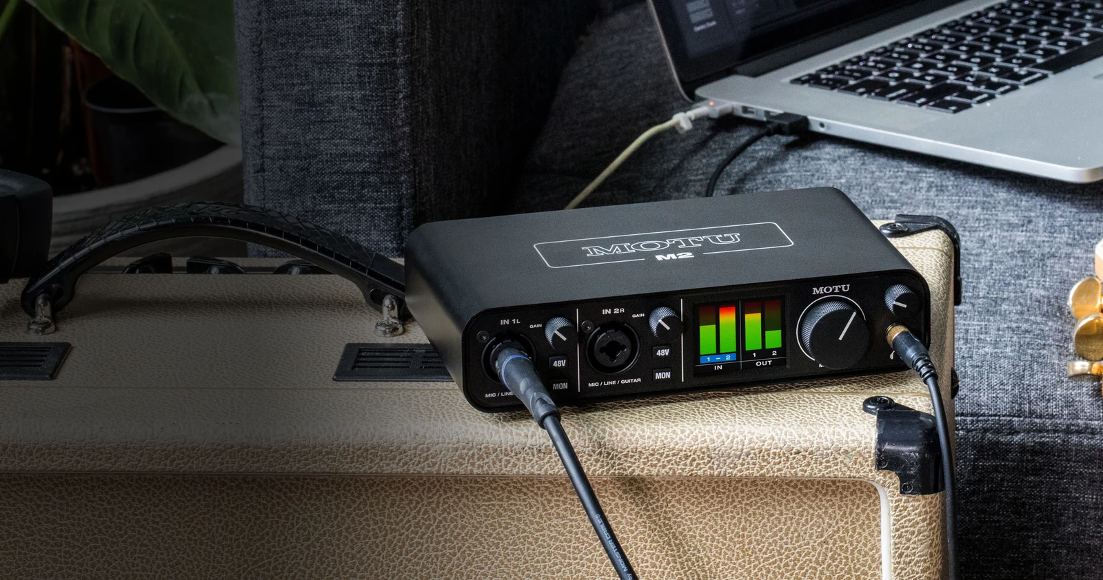 MOTU M2 audio interface shows cables plugged in while sitting on a guitar amp beside a laptop