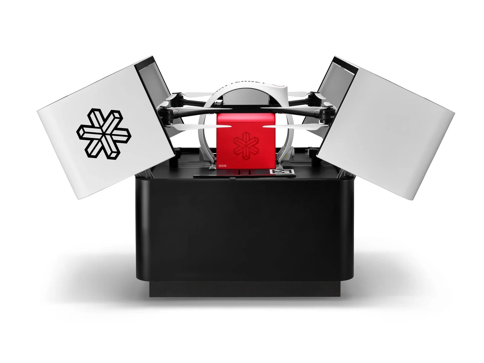 Matternet M3 shows drone delivery hardware: a drone with a red parcel box on a black station with white lids