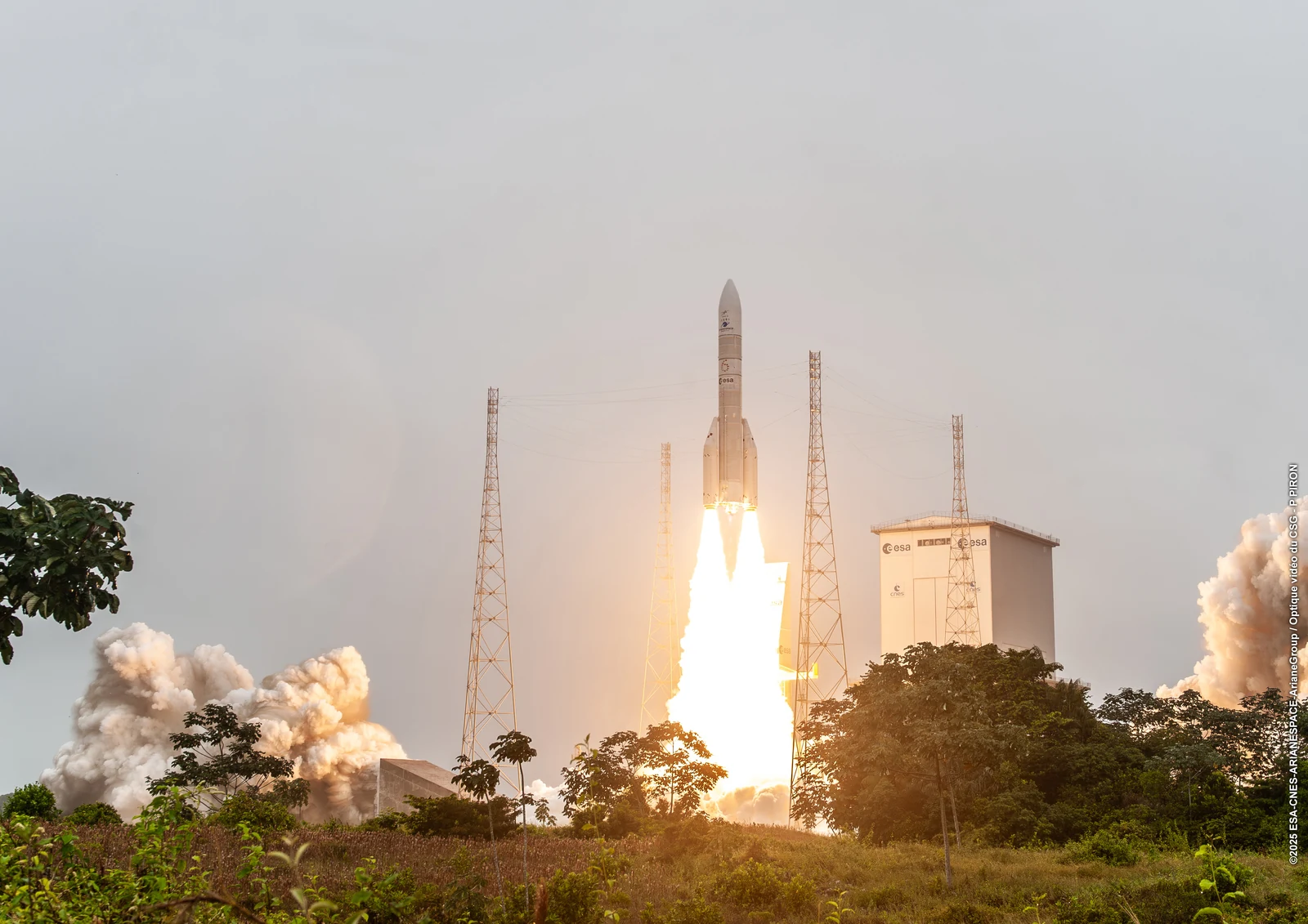 Ariane 6 rocket lifting off shows a commercial space launch among towers, trees and exhaust clouds