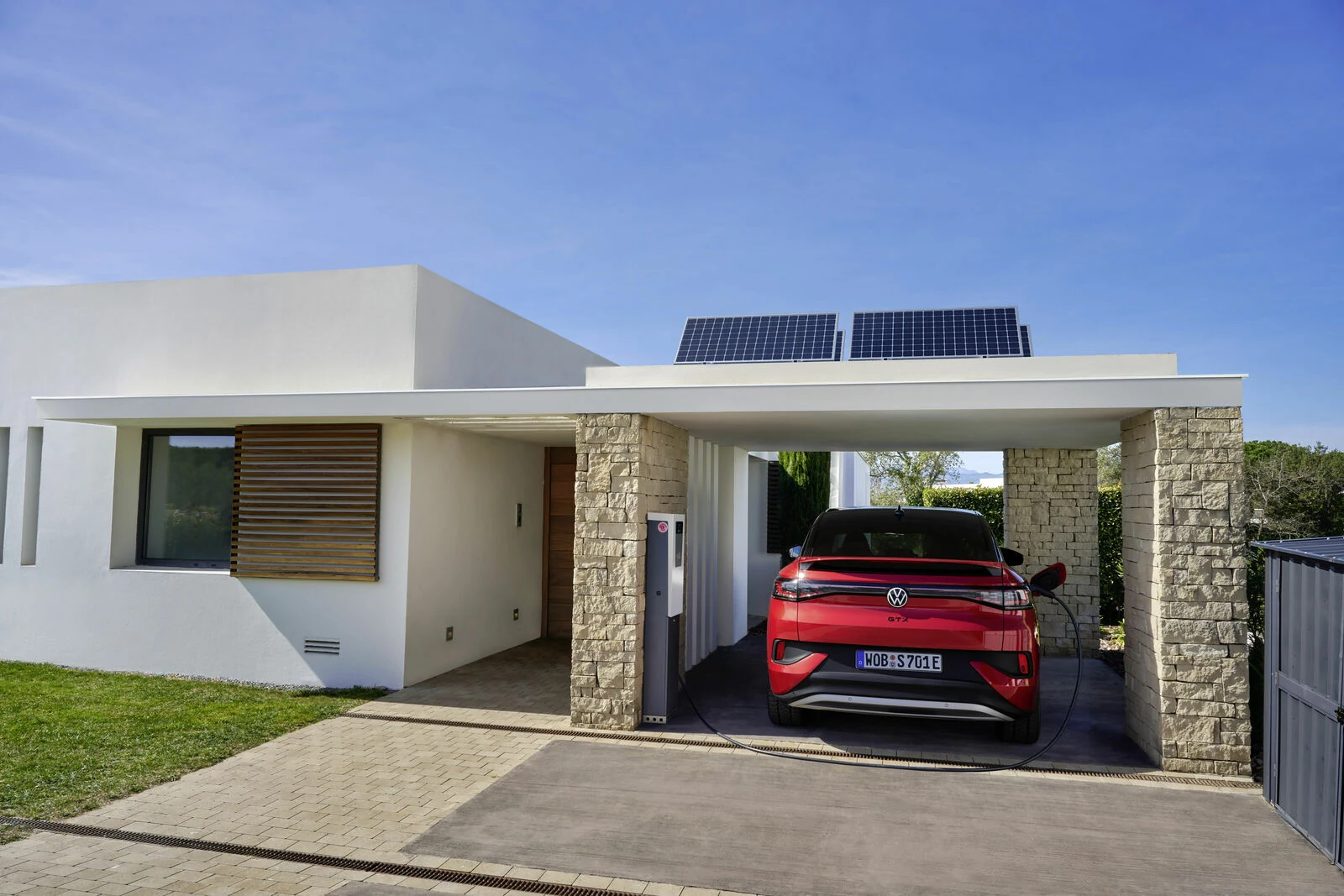 Red Volkswagen ID.4, a software-defined vehicle, shows home charging from a wallbox under a solar carport