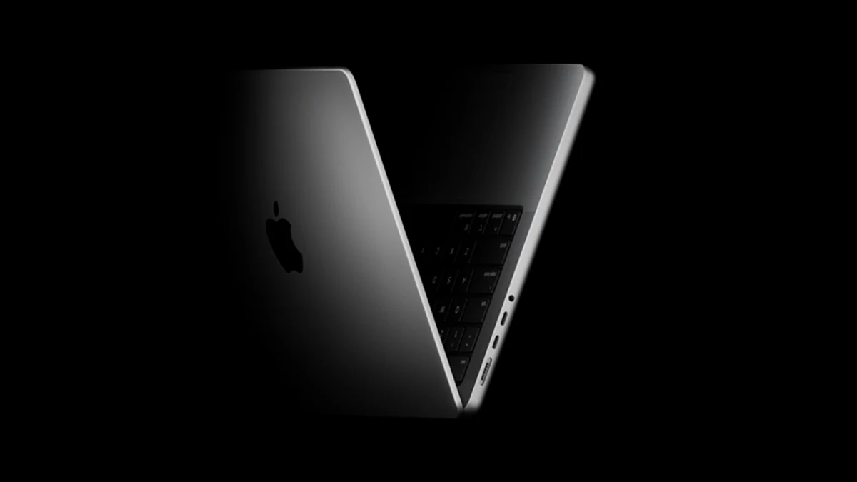 MacBook Pro half open on black, its Apple logo lid and keyboard lit from the side