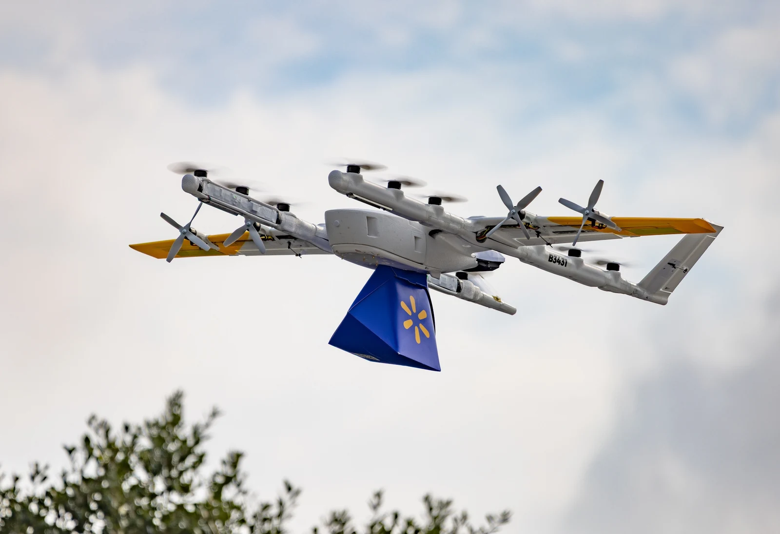Wing drone shows drone delivery in flight, carrying a Walmart-branded package under a cloudy sky