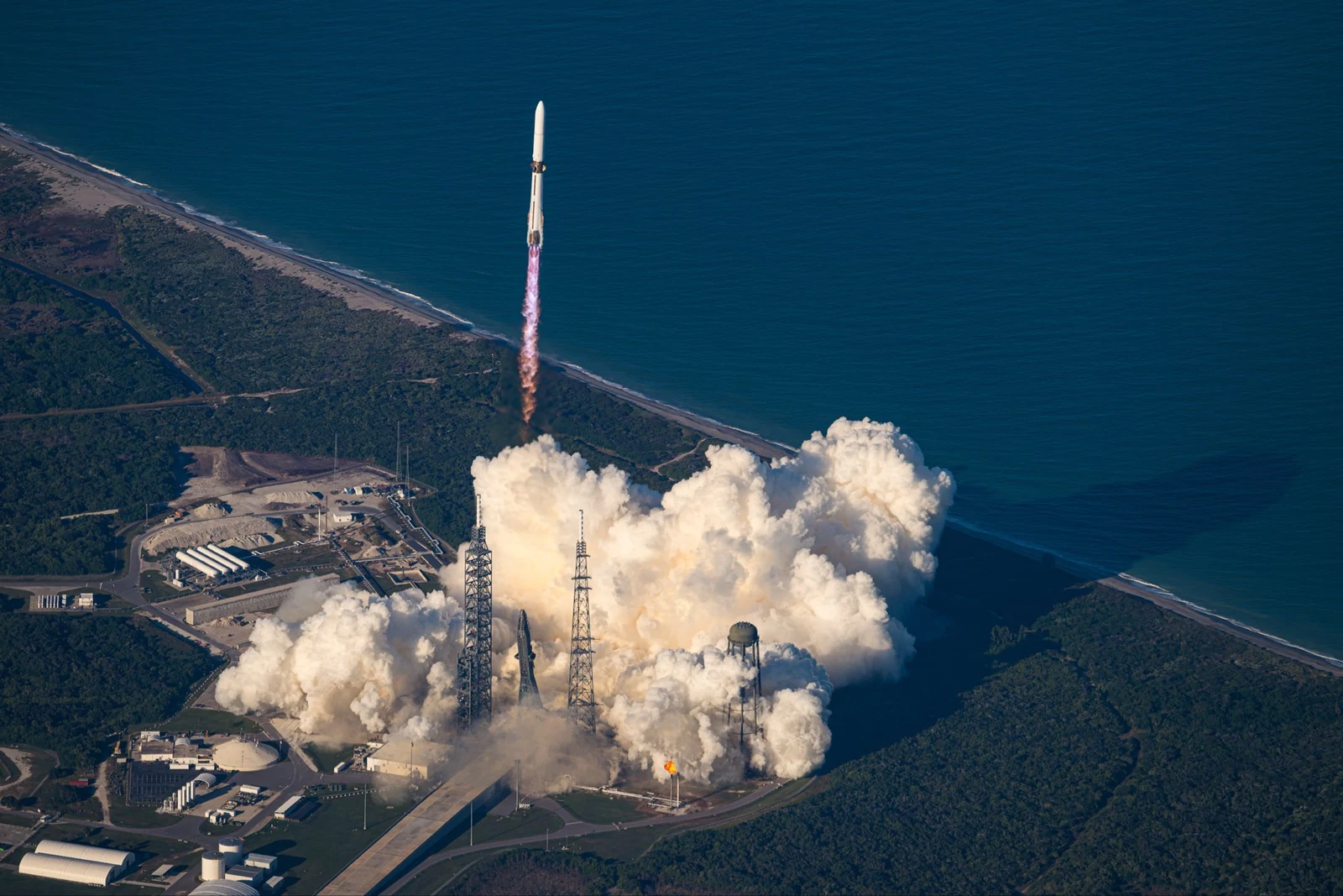 Aerial view shows a New Glenn commercial space launch from a coastal pad with billowing exhaust clouds
