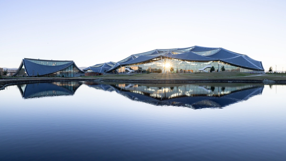Google's Bay View campus in Mountain View, with curved blue canopy roofs reflected in a pond at dusk