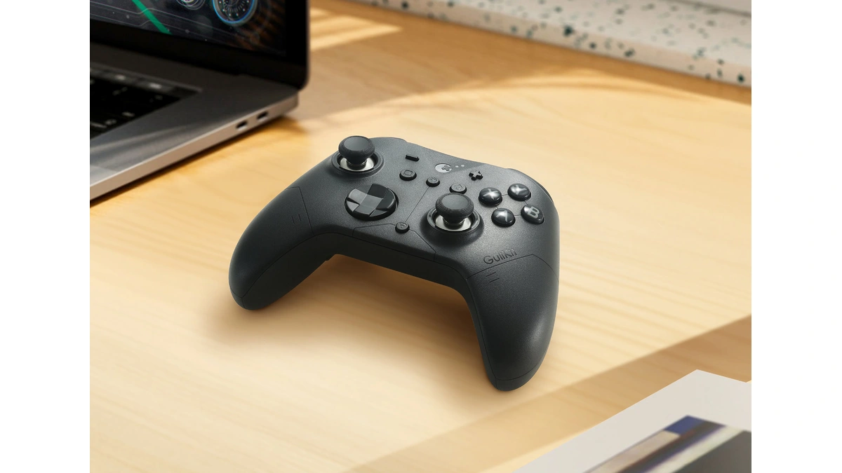 GuliKit ES Max black wireless controller on a wooden desk beside a laptop