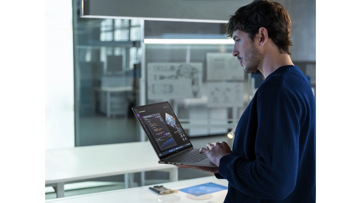 Man holding an open HP laptop and typing in a bright office with glass walls