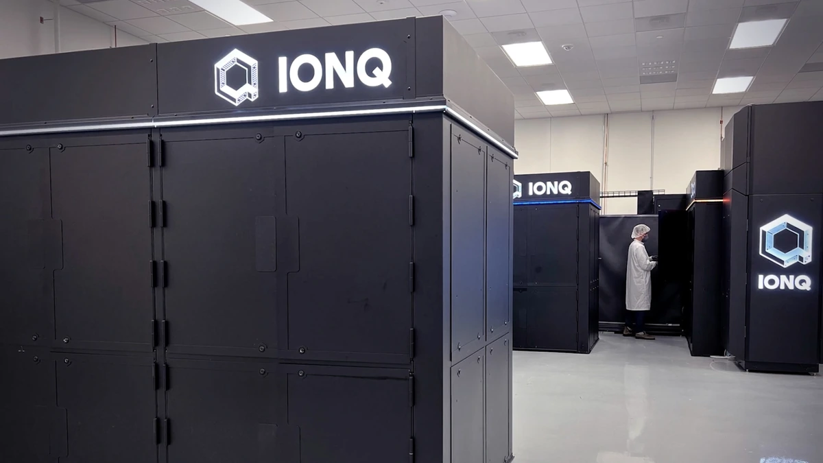 Black IonQ-branded quantum computing cabinets in a lab, with a worker in a white coat at the far end.