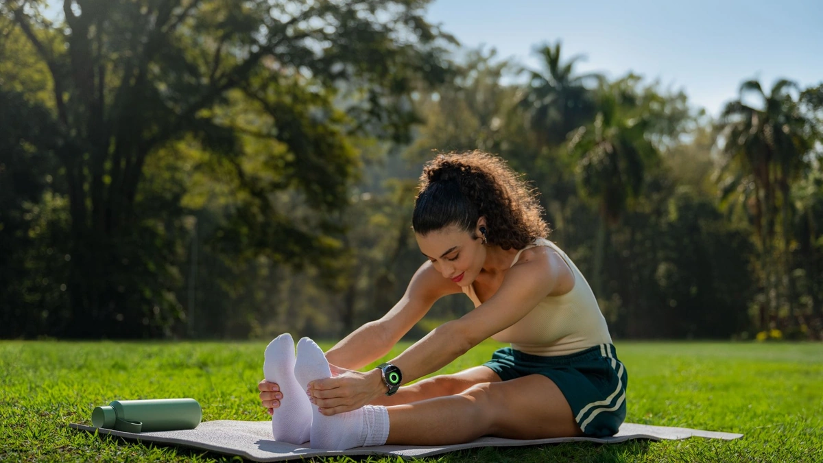 A woman stretching on a yoga mat in a sunlit park with a Motorola smartwatch on her wrist