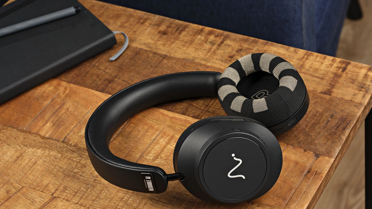 Neurable One headphones with knit striped ear pads resting on a wooden table beside a black notebook and pen