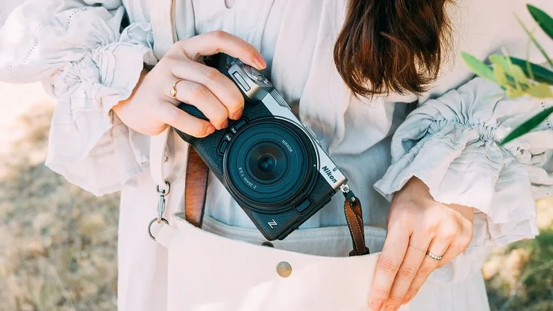 Nikon Z5IIC camera in black held in a person's hand, with a leather strap and a light-colored outfit behind it