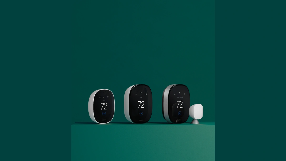 Three Ecobee smart thermostats and one Ecobee room sensor on a green surface against a green wall.