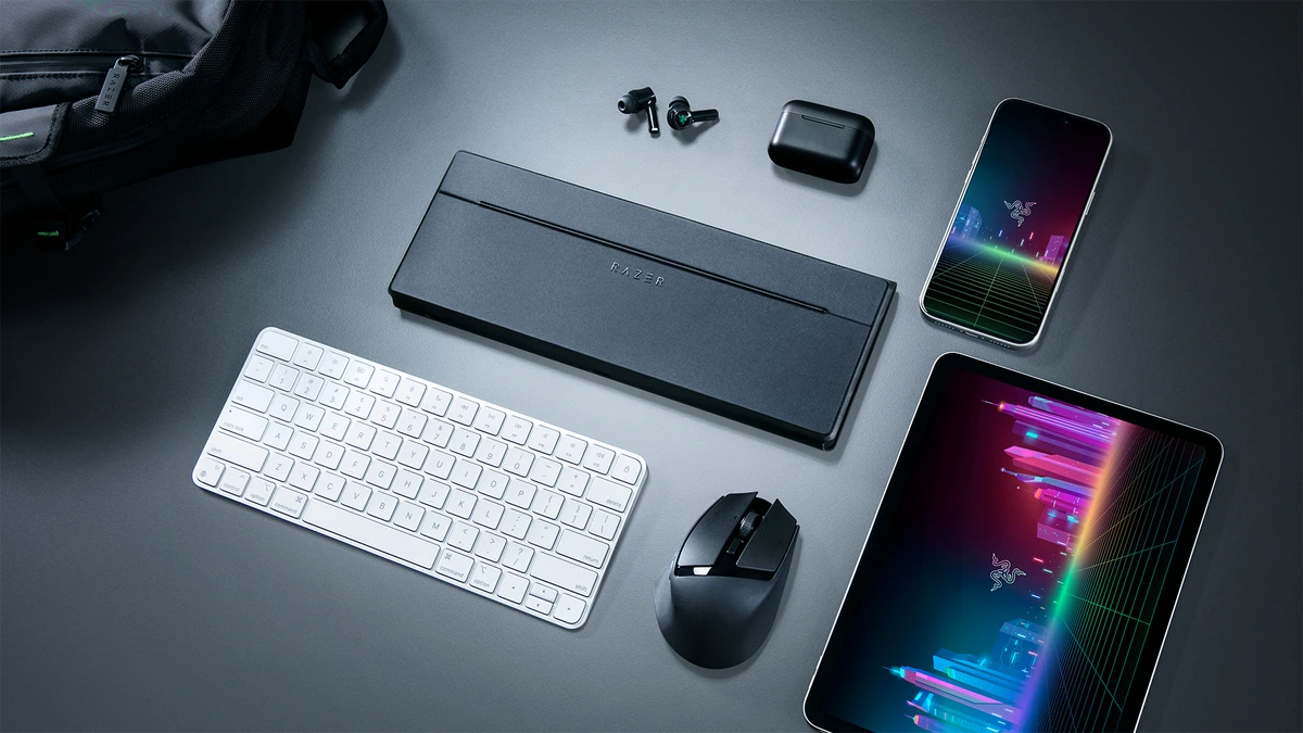 Razer Travel Case Folio closed beside a white keyboard, mouse, earbuds, phone and tablet