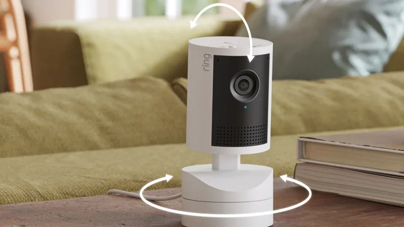 Ring Pan-Tilt Indoor Cam 2K on a wooden table with white arrows showing how it pans and tilts