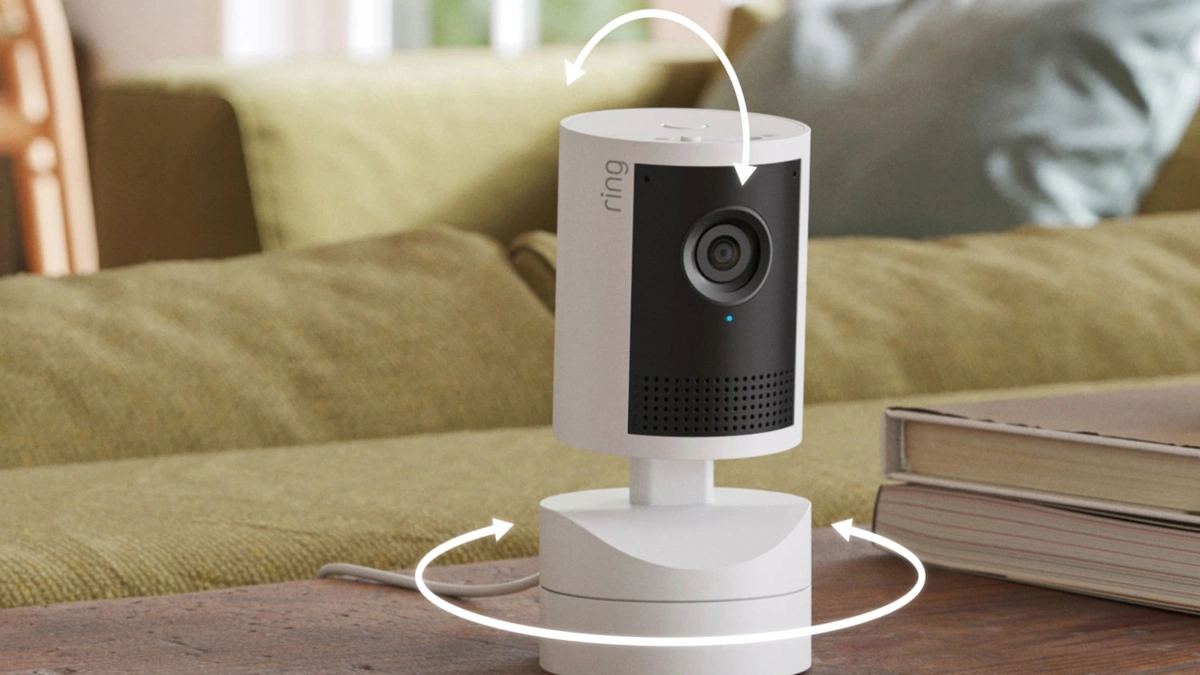 Ring Pan-Tilt Indoor Cam 2K on a wooden table with white arrows showing how it pans and tilts