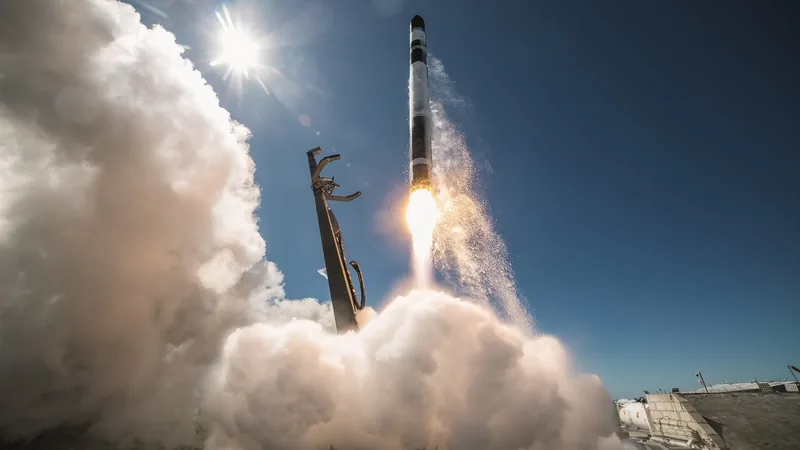 Rocket Lab Electron rocket lifting off with a plume of smoke and flame against a blue sky