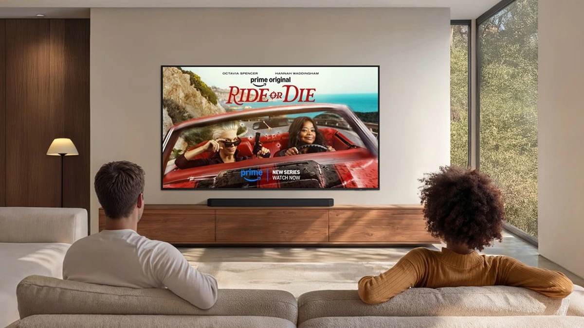 Two people on a sofa watch a wall-mounted Samsung TV showing a Prime Video series in a bright living room.