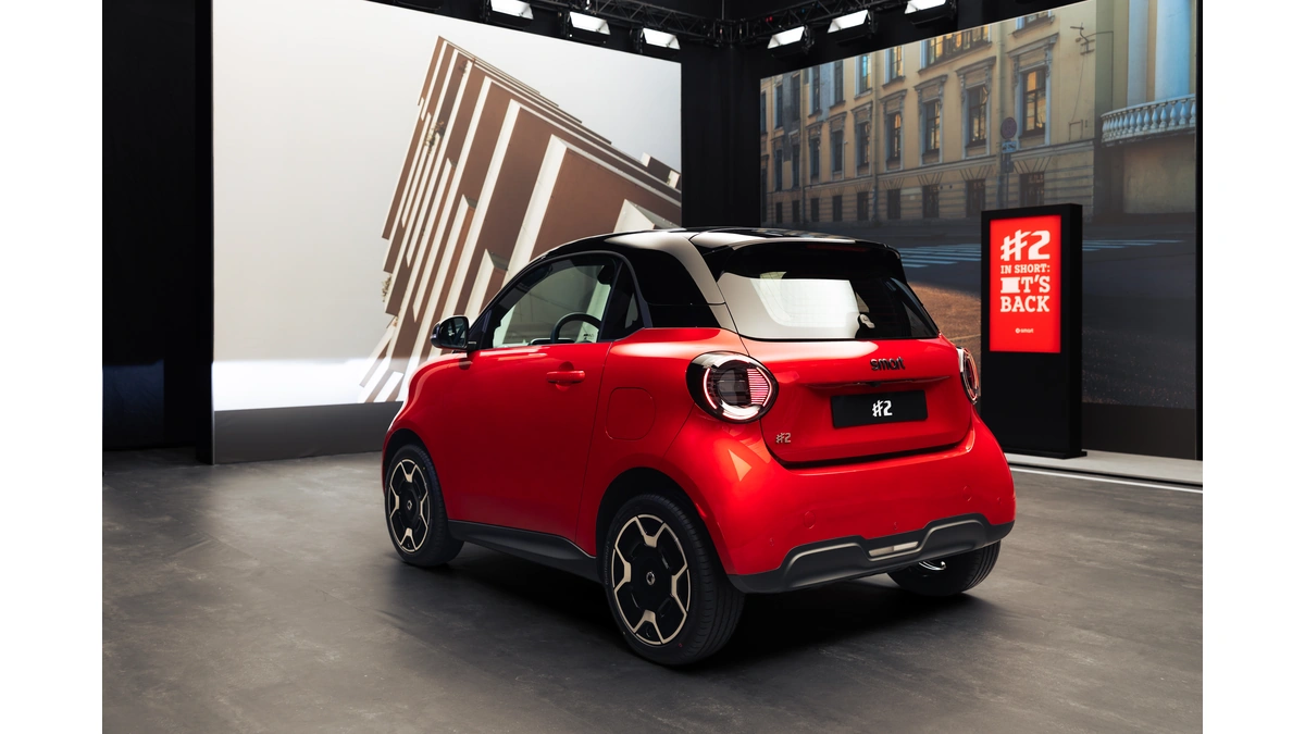 Red smart #2 city car seen from the rear three-quarter in a studio, with a #2 display board behind it