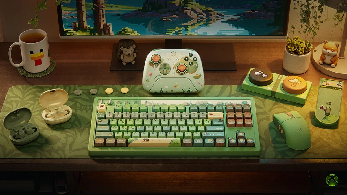 Forest-green Xbox controller, an 8BitDo keyboard and mouse, and earbuds from the Cozy Collection on a leaf-print desk