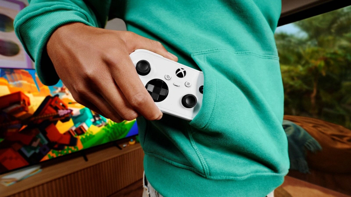 Person in a teal sweatshirt holding a white Xbox Nano Controller in front of a colorful television